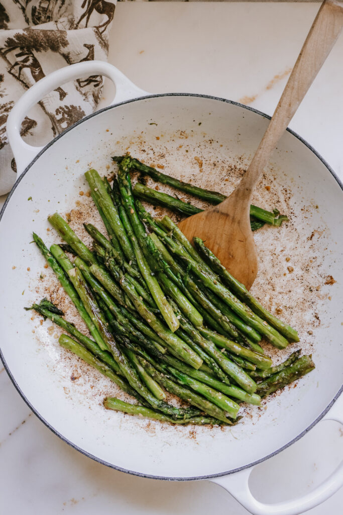 Pan fried asparagus with garlic cooking in a white cast iron skillet