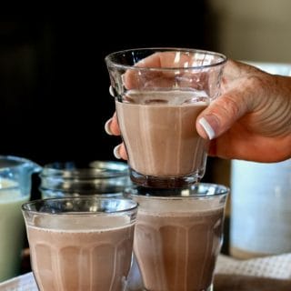 a hand holding a glass of homemade chocolate milk made with cocoa powder