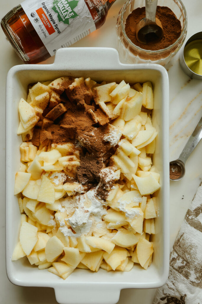 Maple syrup, cinnamon, and flour added to diced apples before mixing
