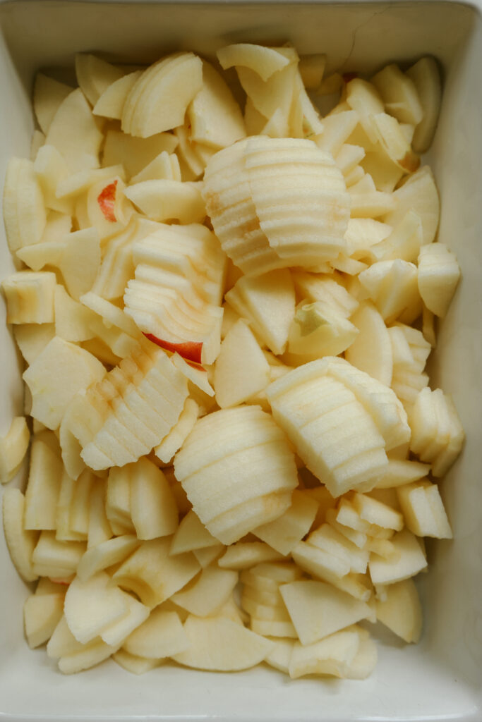 Diced peeled apples filling a casserole dish for healthy apple crisp with maple syrup
