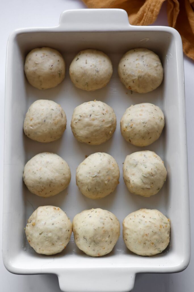 12 rosemary rolls rising in white casserole dish