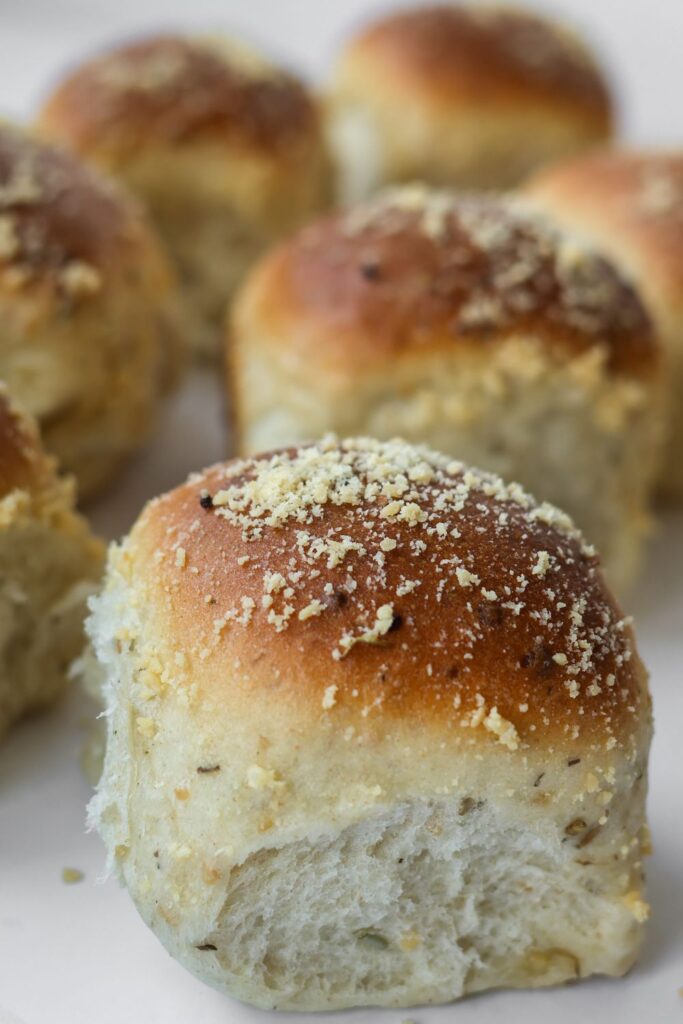 Close-up of warm, buttered rolls with flecks of rosemary and garlic and topped with parmesan cheese.