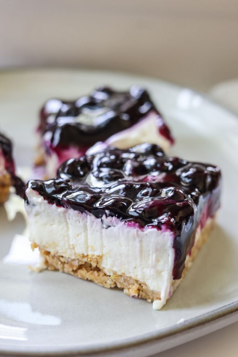 A slice of no bake blueberry lemon cheesecake bar served on a plate, topped with juicy blueberries