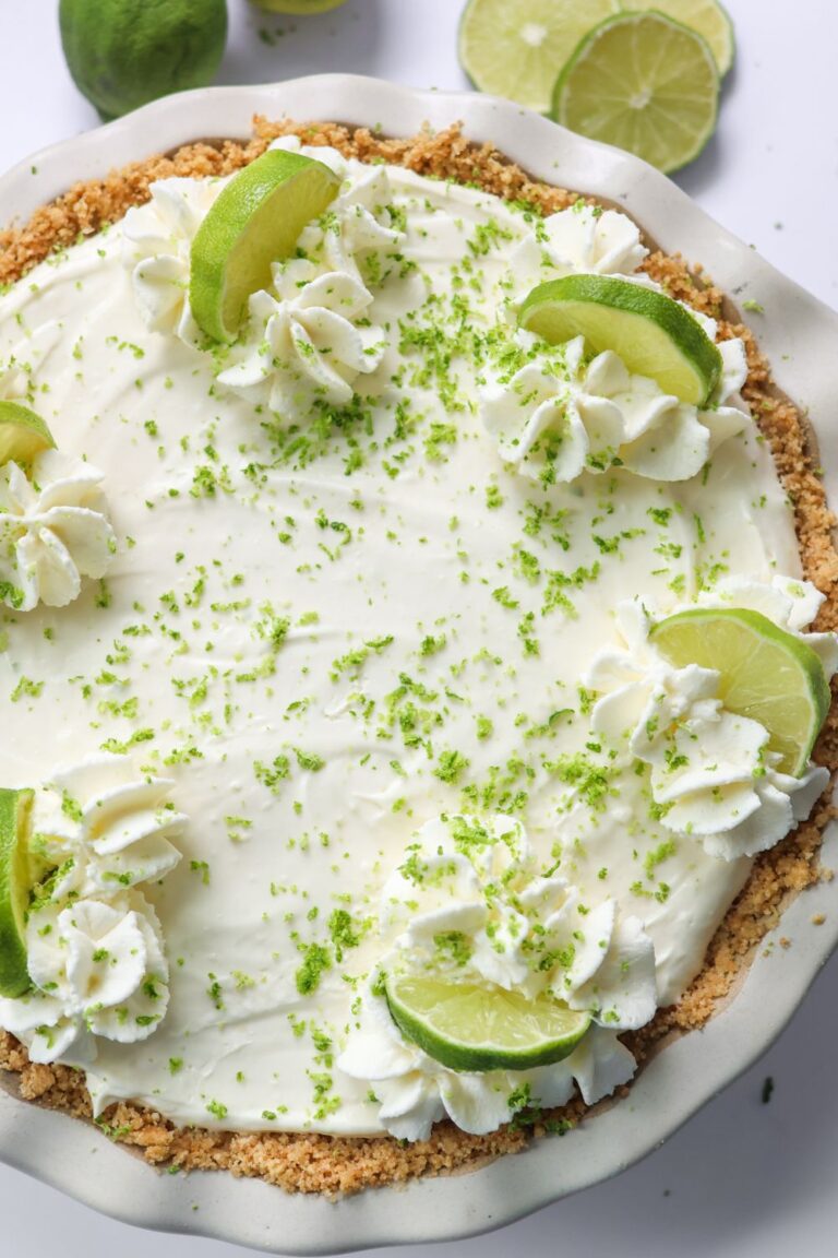 Overhead view of no bake key lime pie with whipped cream border and lime wedges on top.