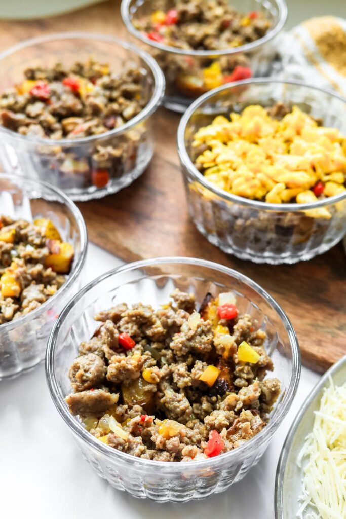 Easy breakfast bowls packed in make-ahead containers with scrambled eggs, breakfast sausage, and cheese.