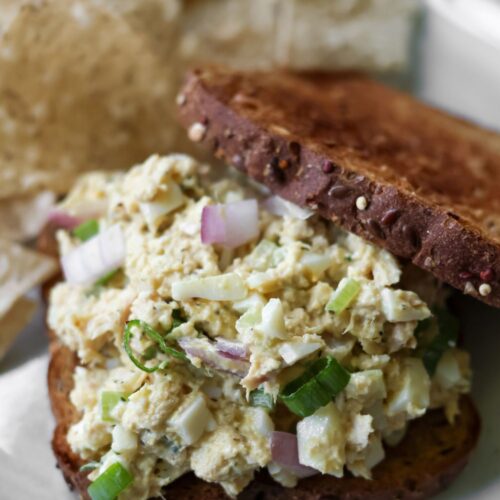Close-up of two pieces of toast spread generously with cottage cheese tuna salad, showing a creamy texture with visible chunks of tuna and herbs.
