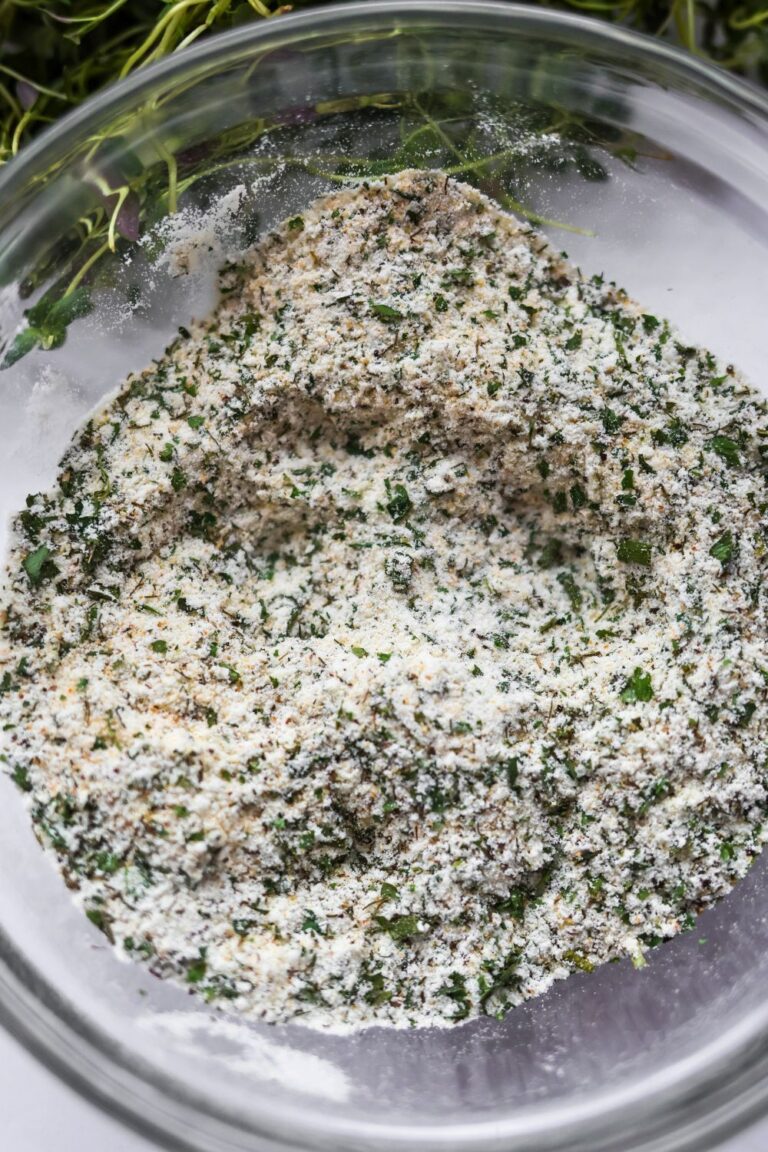 Homemade ranch seasoning mix in a glass bowl with visible flecks of green herbs and powdered spices, partially stirred.