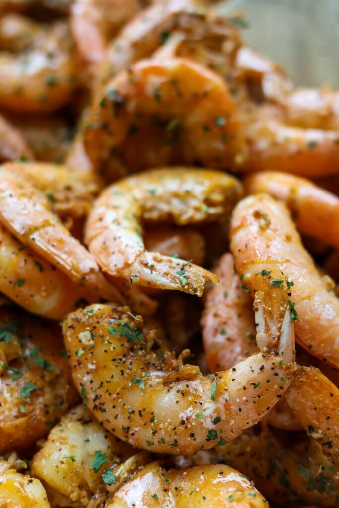 Close-up of juicy, pan-cooked Old Bay peel and eat shrimp, seasoned with garlic, black pepper, and parsley flakes.