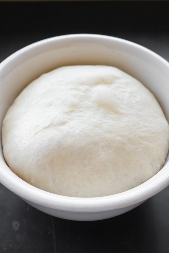 Homemade pizza dough recipe with all-purpose flour after first rise in a white bowl, smooth airy texture for the best chewy and crispy pizza crust.