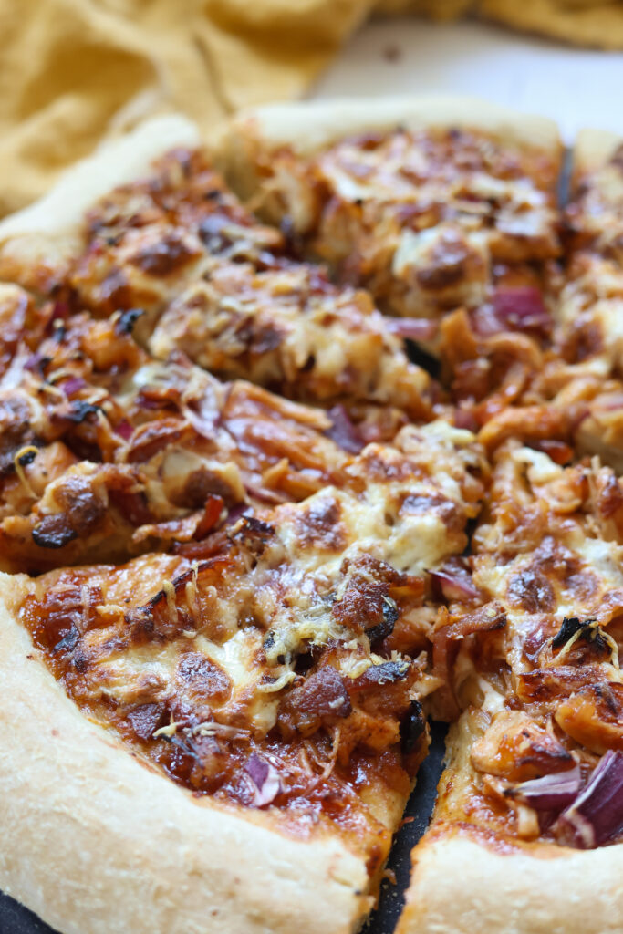 Golden brown BBQ chicken bacon pizza fresh out of the oven with melted mozzarella cheese, crispy bacon, caramelized red onions, and a sprinkle of parmesan cheese