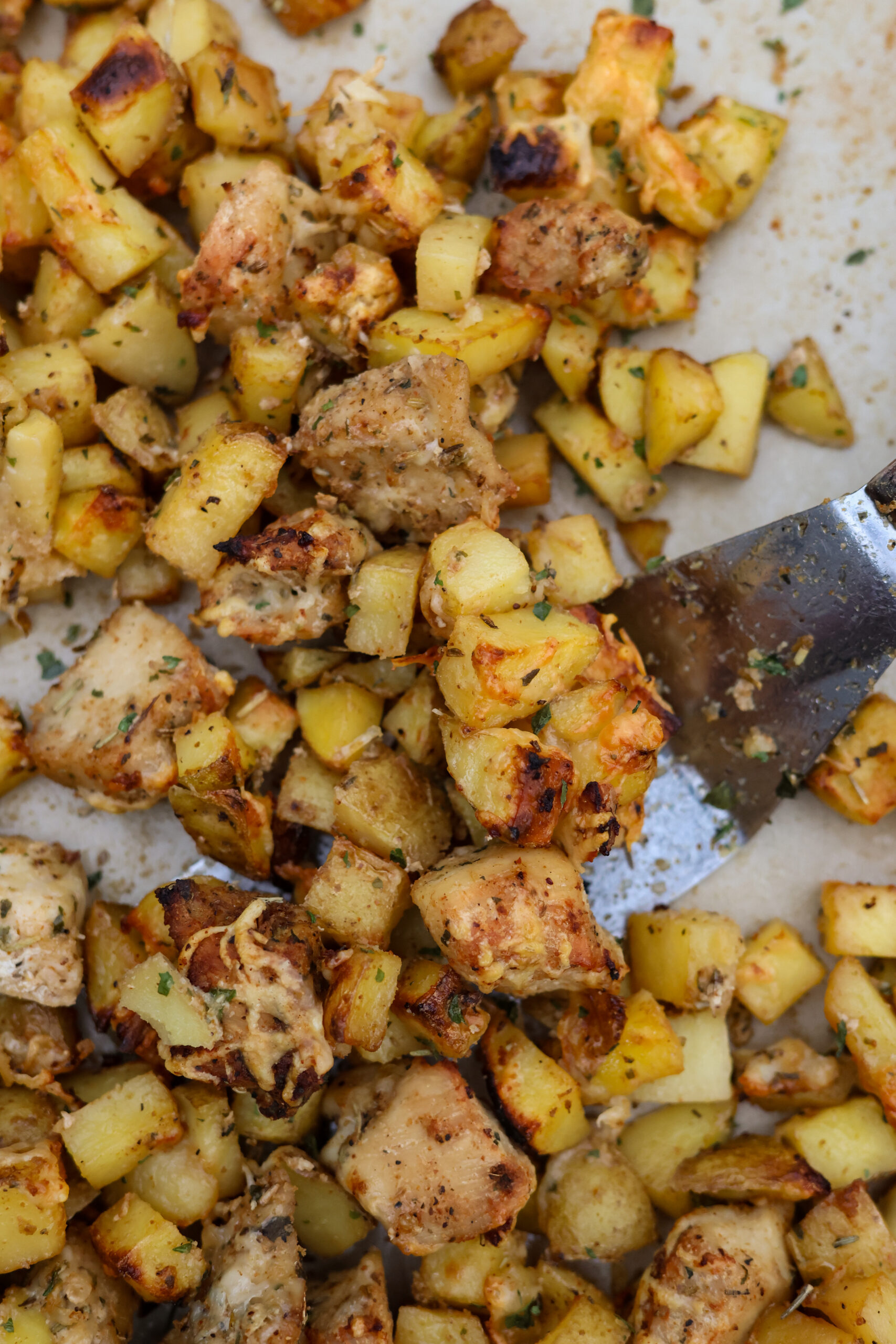Close-up of juicy chicken pieces and crispy potatoes with a sprinkle of herbs and melted cheese, fresh from the oven.