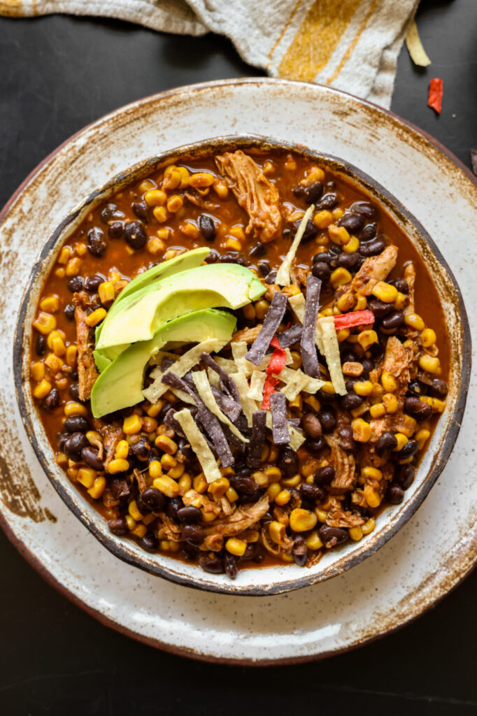 Close-up of chicken enchilada soup topped with fresh avocado and tortilla strips in a handmade pottery bowl.