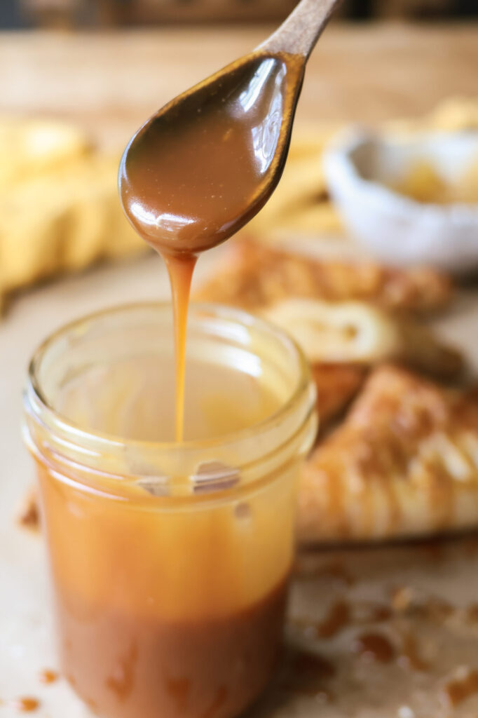 Thick, golden homemade caramel sauce in a jar with a spoon ready to serve