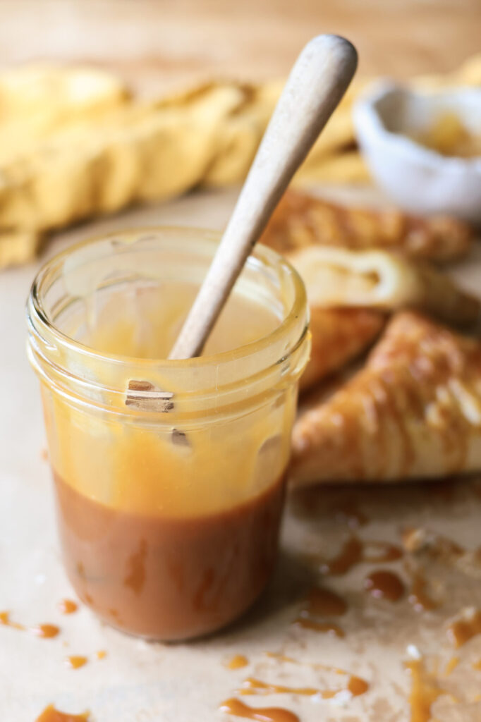 Jar of creamy homemade caramel sauce with a spoon dripping caramel