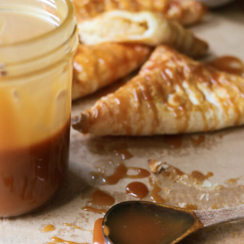 Close-up of homemade caramel sauce in a jar and on a spoon, perfect for drizzling