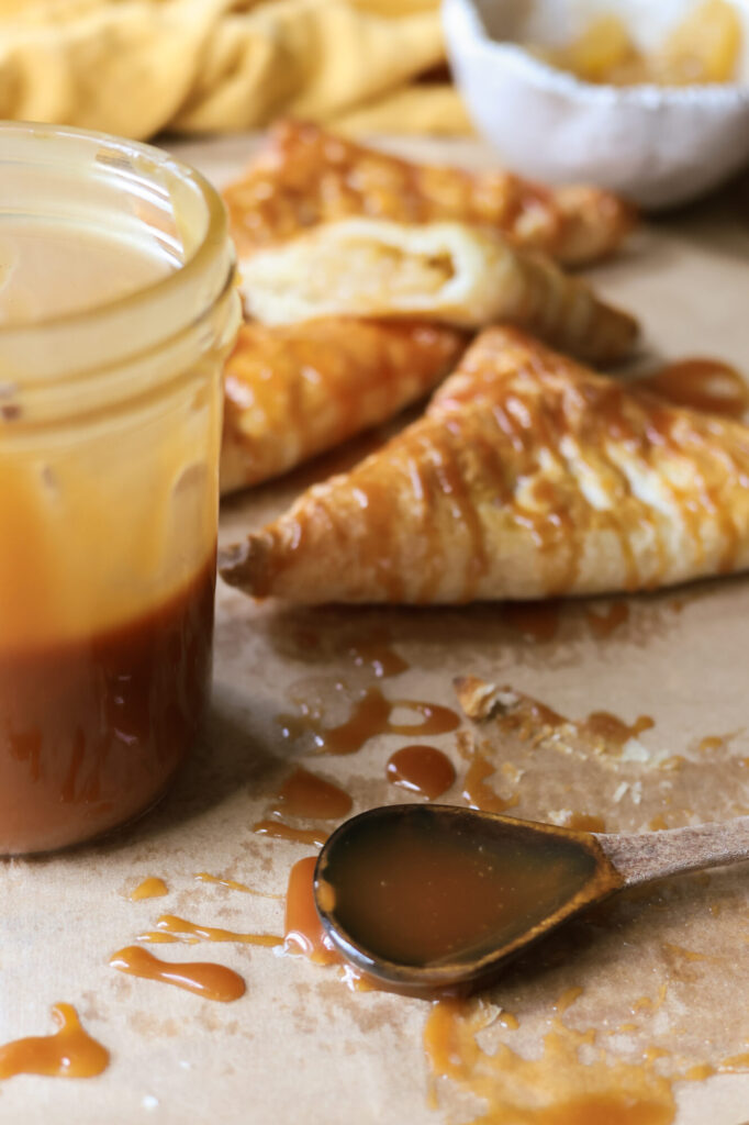 Close-up of homemade caramel sauce in a jar and on a spoon, perfect for drizzling