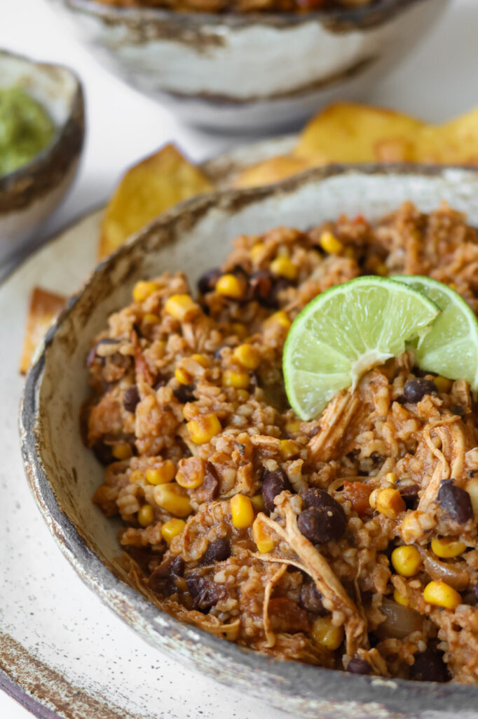 Freshly cooked crock pot chicken and rice with Mexican flavors in ceramic bowl with limes on top.