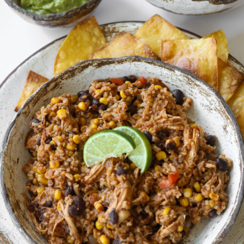 Slow cooker Mexican chicken and rice served in a rustic pottery bowl with lime garnish on top.