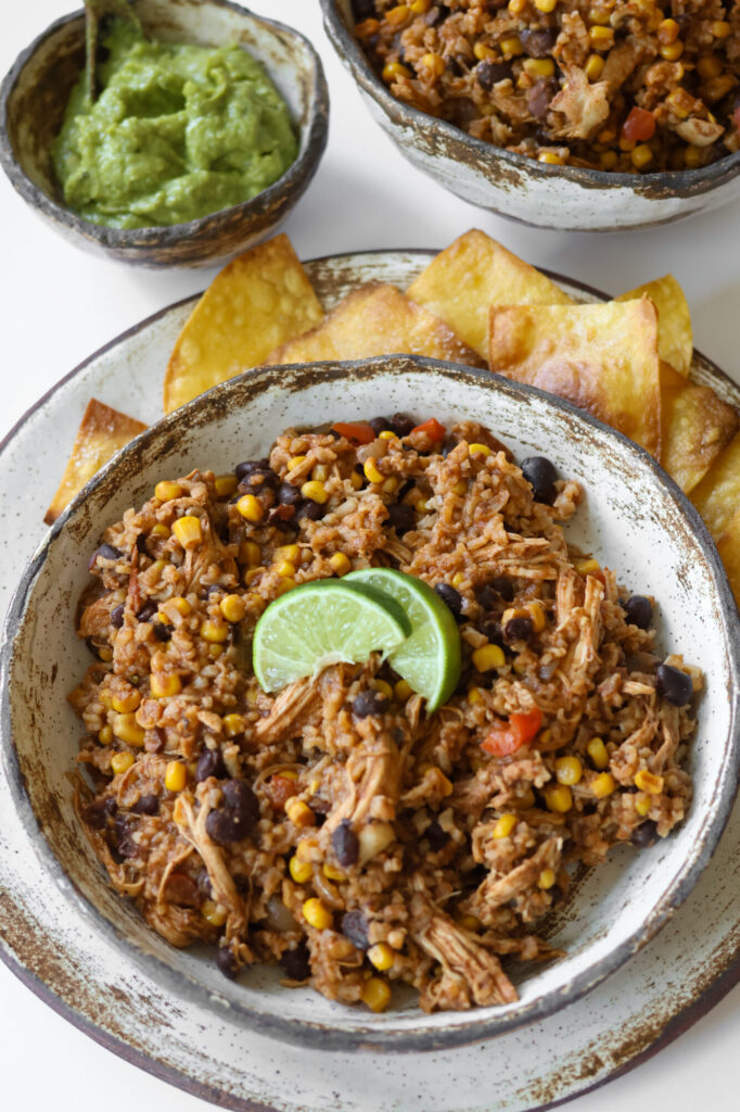 Slow cooker Mexican chicken and rice served in a rustic pottery bowl with lime garnish on top.