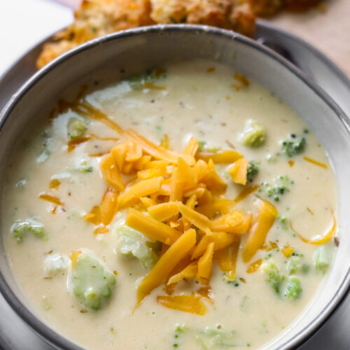 Creamy broccoli cheddar soup in a bowl topped with melted cheese and fresh broccoli.