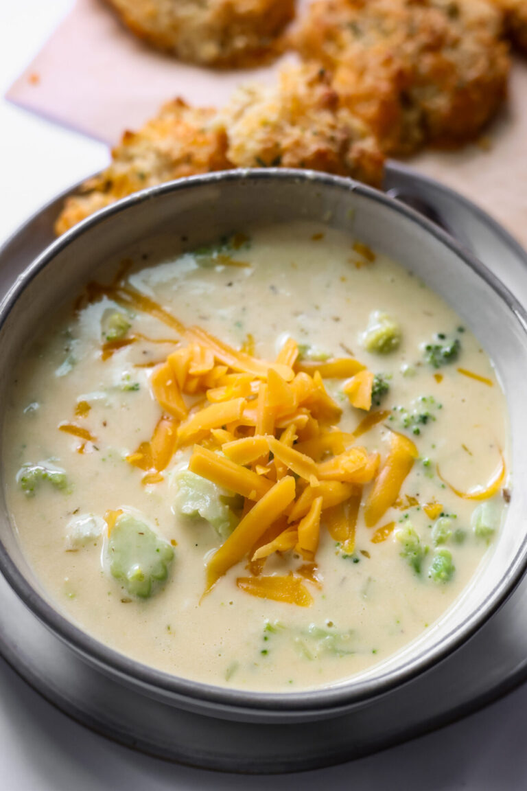 Creamy broccoli cheddar soup in a bowl topped with melted cheese and fresh broccoli.