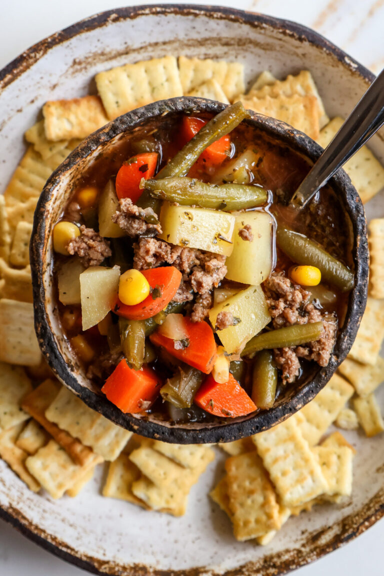 Bowl of hot vegetable soup with ground beef, carrots, potatoes, green beans, and corn, served with crackers.