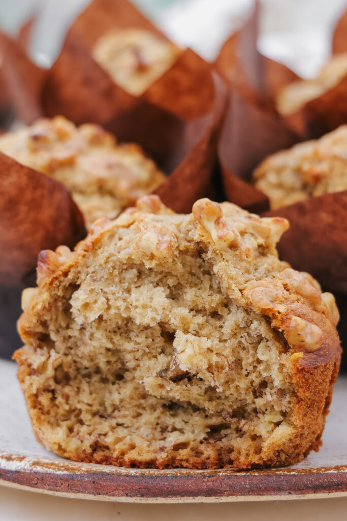 Banana muffin with sour cream split open showing a moist tender crumb with walnuts on a ceramic plate.