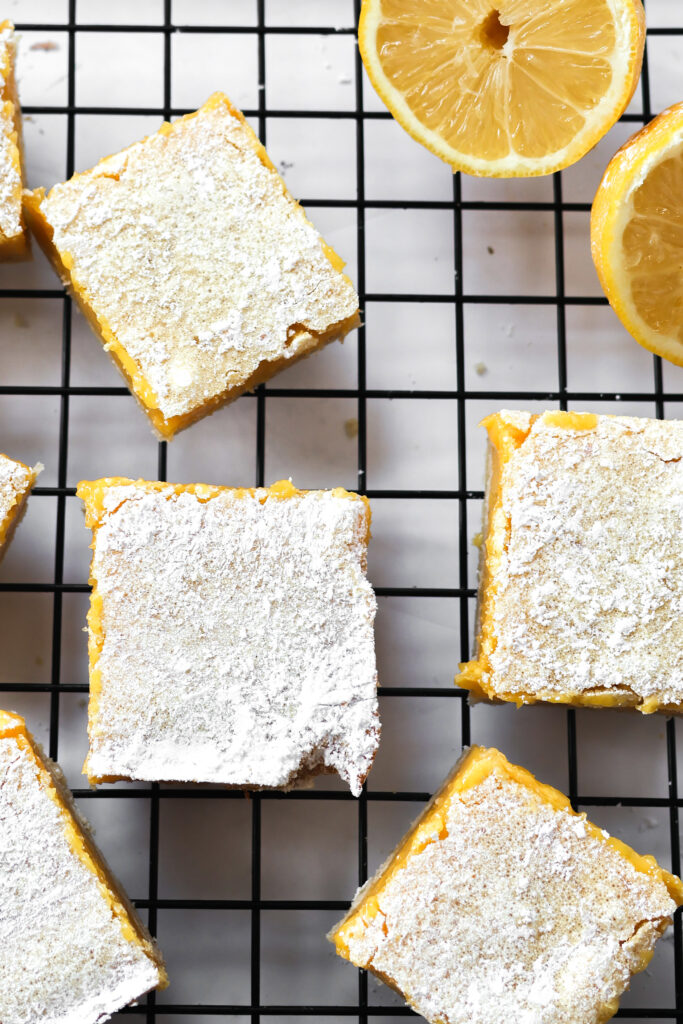 Overhead view of dessert bars made with lemon on a wire rack with sliced lemons.