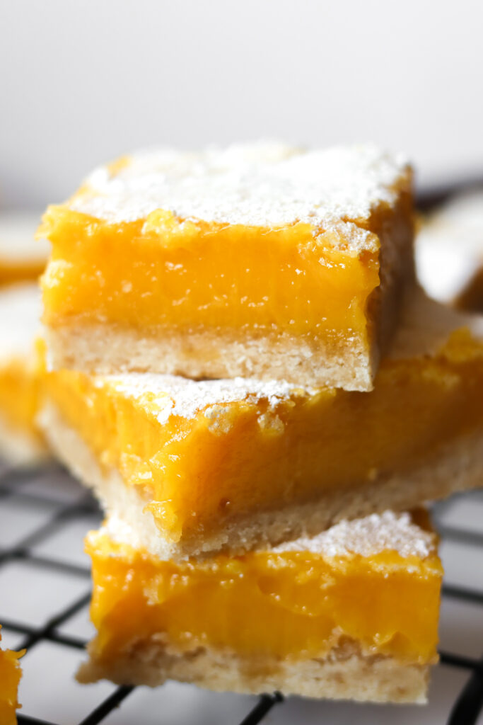 Stacked lemon bars on a wire rack with fresh lemons in the background
