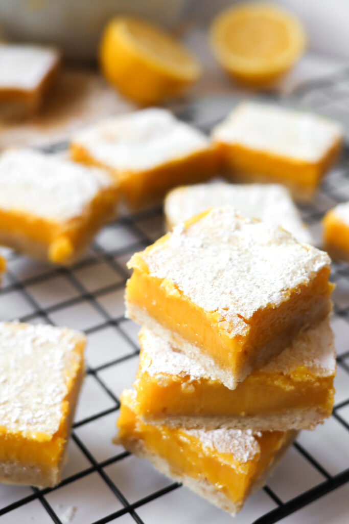 Lemon bars stacked on a wire rack with fresh lemons in the background.
