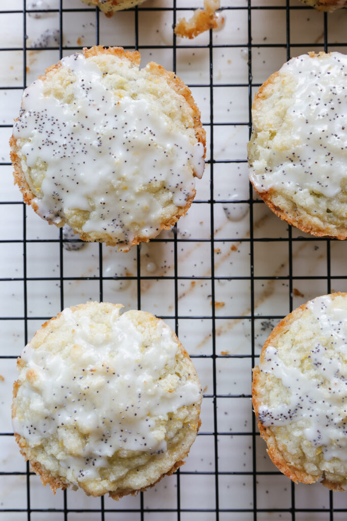 Overhead close-up of jumbo lemon poppy seed muffins with glossy lemon glaze dripping down the sides on a black wire rack.
