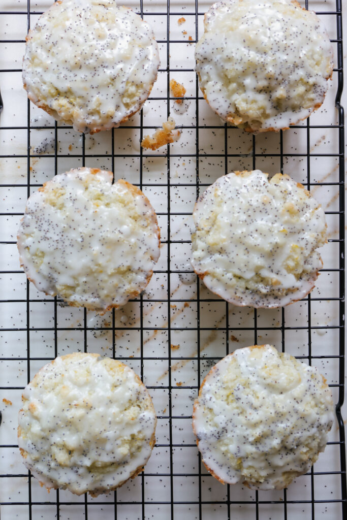 Six jumbo lemon poppy seed muffins with lemon streusel and glaze arranged on a black wire rack.