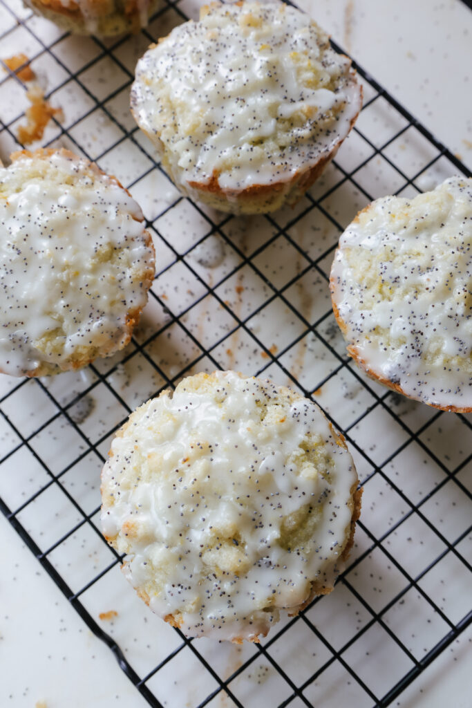 Angled close-up of glazed muffins with crumbly streusel topping on a wire rack.