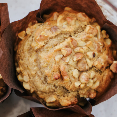 Overhead view of a bakery style banana walnut muffin sweetened with maple syrup in a brown parchment wrapper