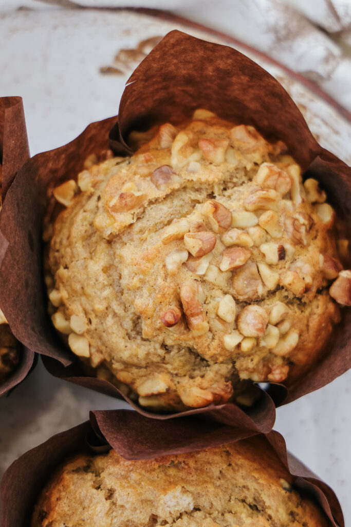 Overhead view of a bakery style banana walnut muffin sweetened with maple syrup in a brown parchment wrapper