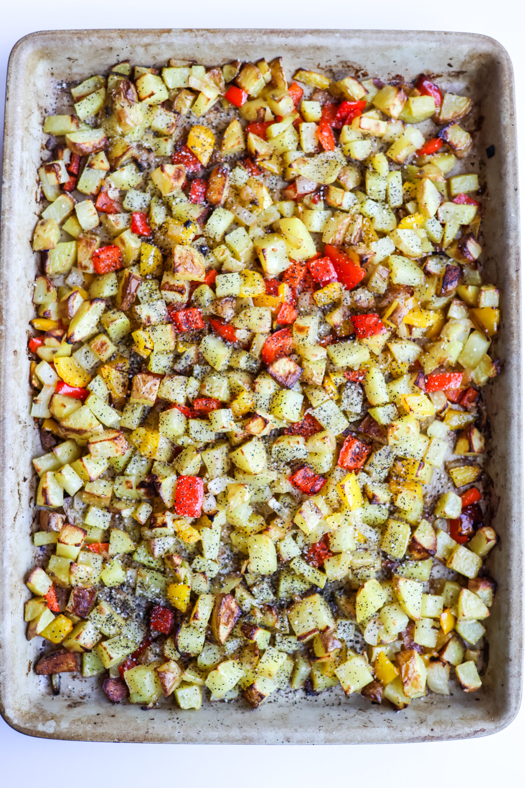 Sheet pan breakfast potatoes with red and yellow bell peppers roasted on a rimmed baking sheet