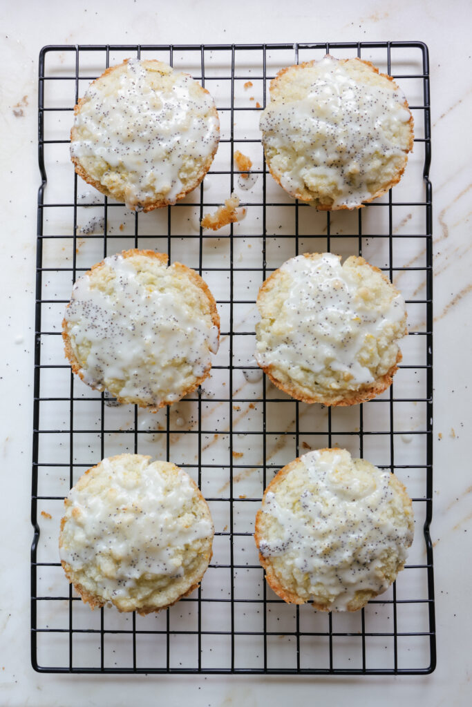 Six glazed muffins cooling on a black wire rack over a marble surface overhead.