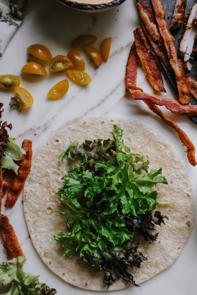 Lettuce, halved cherry tomatoes, crispy bacon, and grilled chicken laid out for a BLT chicken wrap