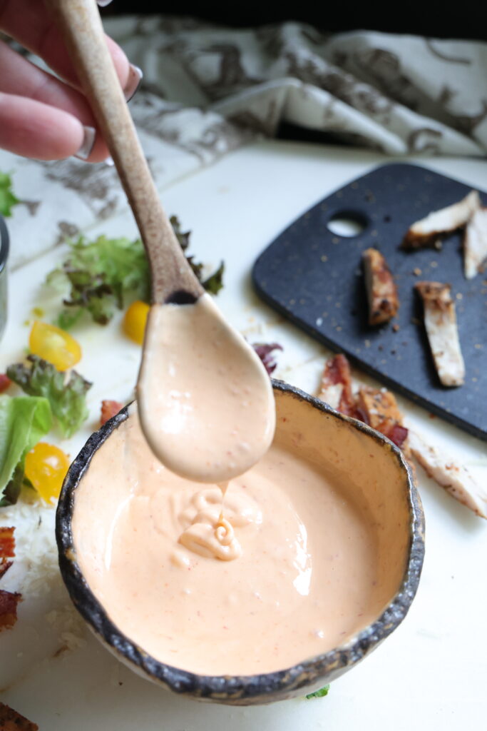 Close-up of thick sriracha mayonnaise dripping off a wooden spoon into a bowl.