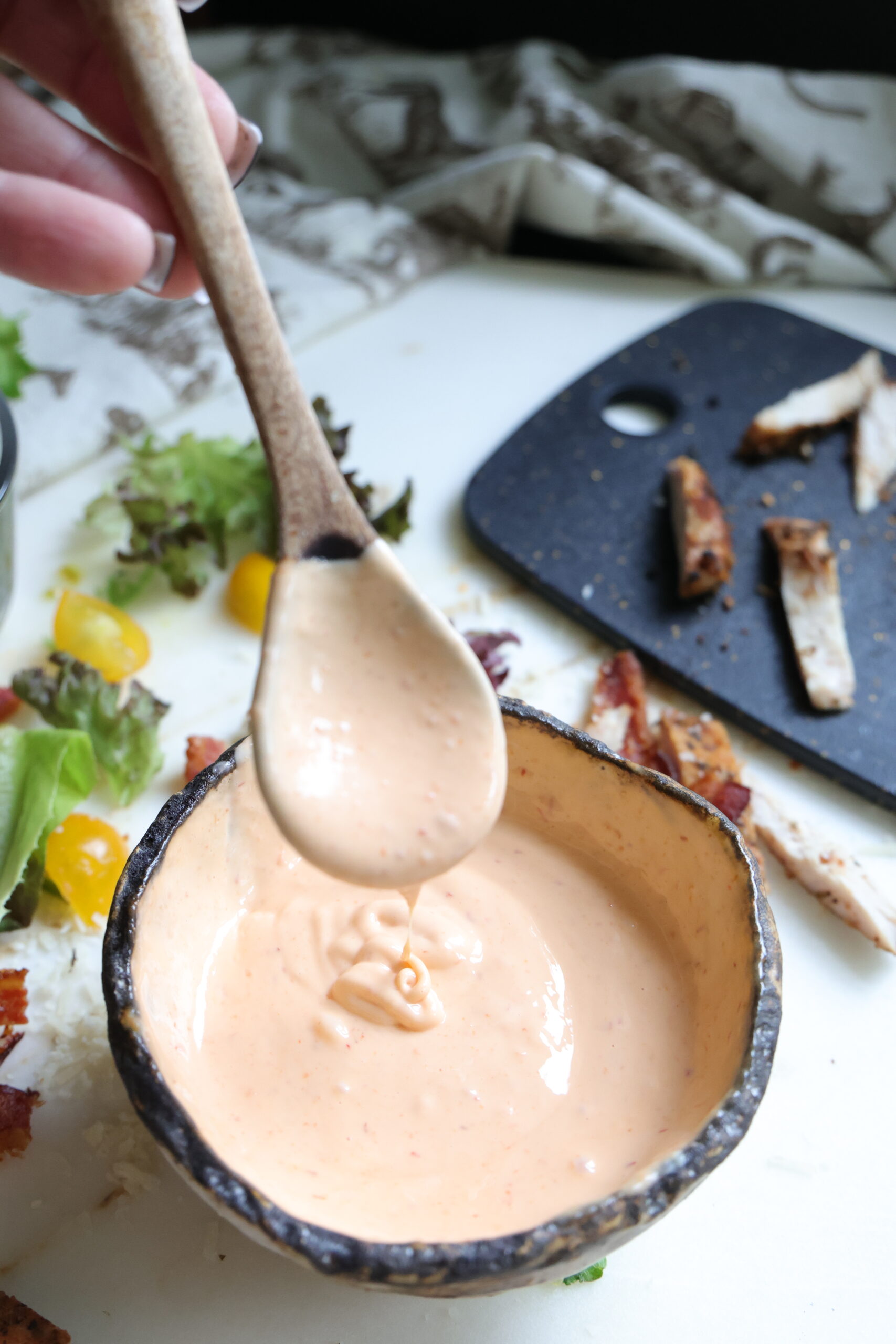 Close-up of thick sriracha mayonnaise dripping off a wooden spoon into a bowl.