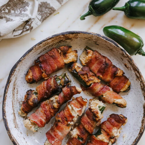 Crispy air fryer bacon wrapped jalapenos on a speckled plate with fresh jalapenos alongside