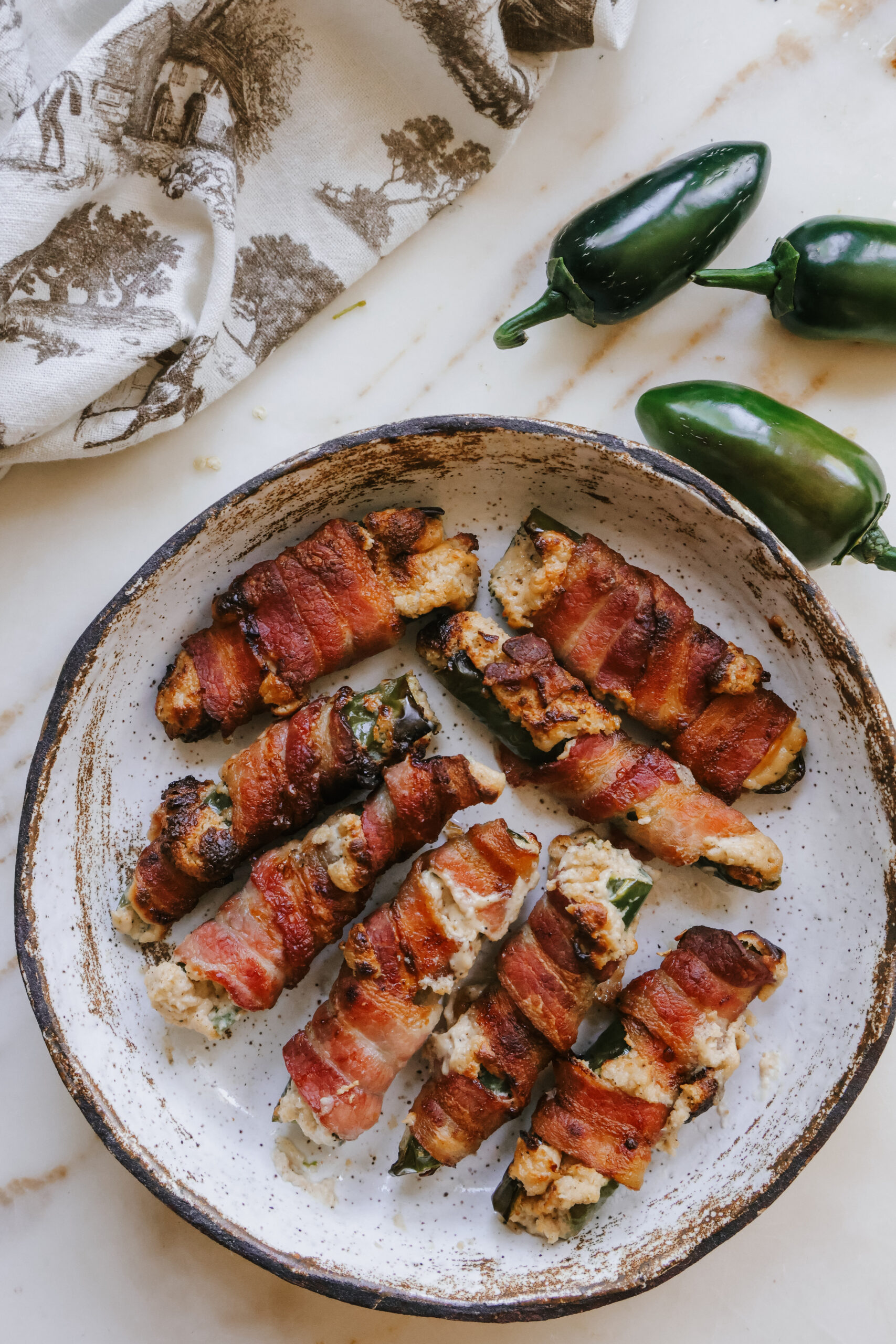 Crispy air fryer bacon wrapped jalapenos on a speckled plate with fresh jalapenos alongside