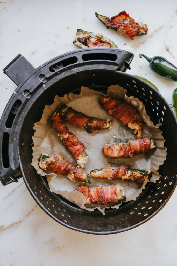Bacon wrapped jalapeno poppers arranged in an air fryer basket lined with parchment