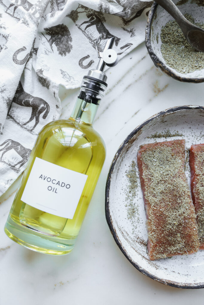 A bottle of avocado oil next to rub-coated salmon fillets ready for the skillet