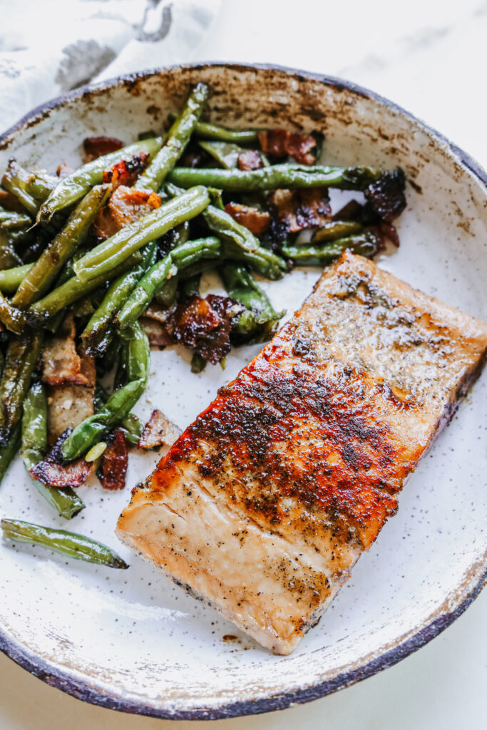 Close-up of a pan fried brown sugar salmon fillet plated with green beans and bacon