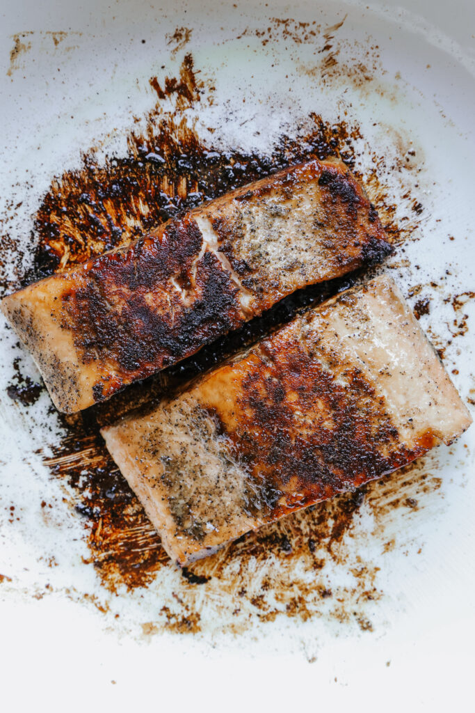 Two salmon fillets with a dark caramelized brown sugar crust in a white skillet