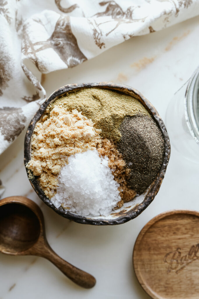 Brown sugar, ground cumin, black pepper, dry mustard, and flaky salt in a rustic bowl before mixing