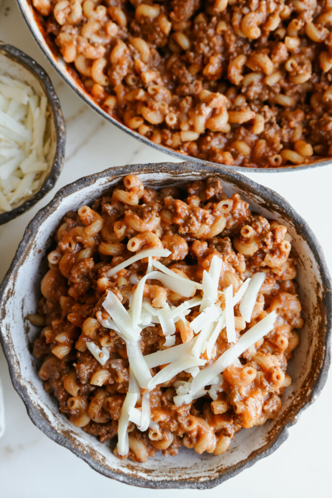 Serving of chili mac with no beans in a rustic stoneware bowl with shredded cheese