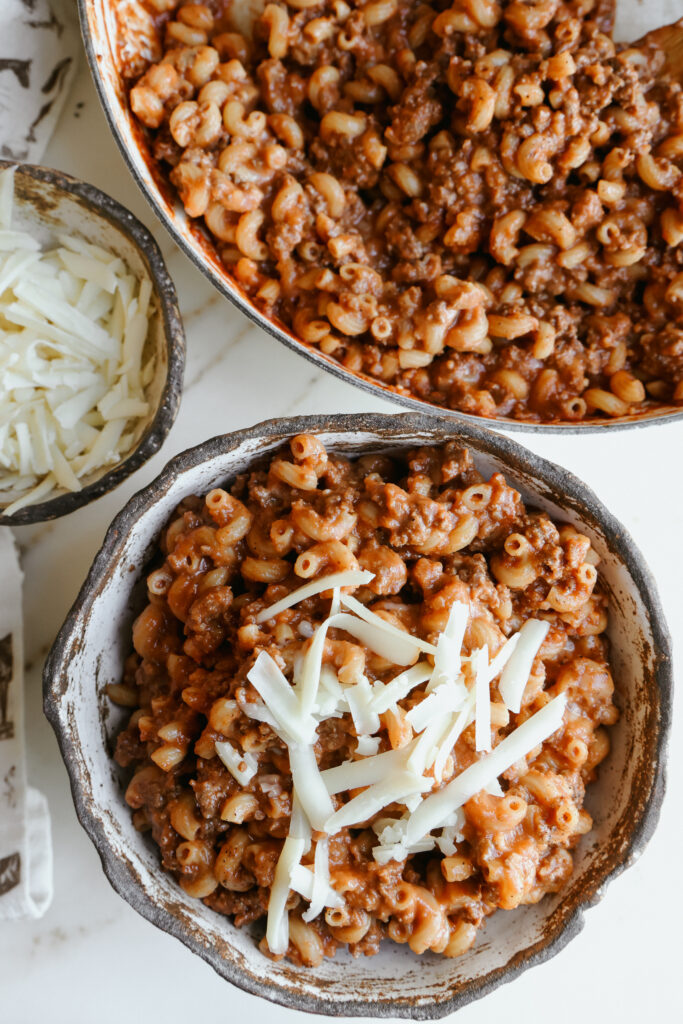 Bowl of homemade chili mac topped with shredded white cheddar