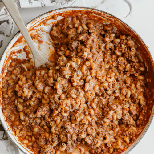 Chili mac without beans in a white cast iron braiser with a wooden spoon
